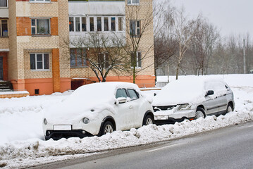 Cars parked on snowy roadside blocked by slush piles, impact of snowplow work during winter storm. Roadside parking zone in residential area with snow covered cars, aftermath of municipal snow removal