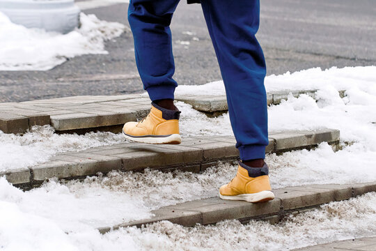 Man in warm boots moving slowly on snowy outdoor steps, safety awareness during cold winter weather, icy conditions. Snowy staircase with man in winter footwear maintaining balance to avoid slipping