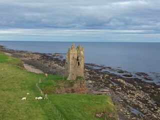 Aerial drone views of Keiss Castle near Wick, reveal its dramatic ruins perched on a rugged cliff above the sea, Scotland UK
