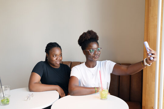 Two young women taking selfie together in a bright modern cafe, representing friendship, social media, connection and positive lifestyle moments.