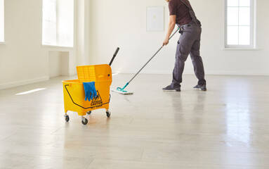 Male janitor in uniform washing floor with caution wet floor sign in empty room or at office. Man...