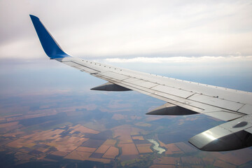 Aerial view of landscape with airplane wing over fields and river under cloudy sky