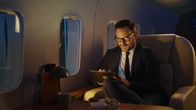 Handsome businessman traveling in first class on a corporate jet. Working on a tablet computer during a comfortable night flight. Luxurious and successful lifestyle concept for a corporate executive