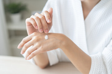 Health care, beauty smile pretty asian young woman in bathrobe, towel after shower bath at home, finger applying moisturizer on her back hand. Skin body cream moisturizing lotion, routine in morning.