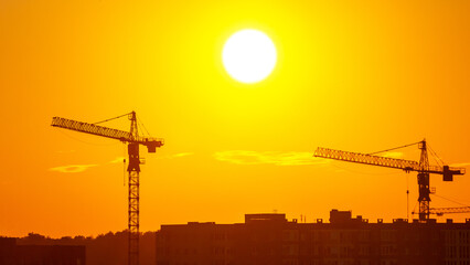 Construction cranes silhouetted against a sunset sky in an urban landscape