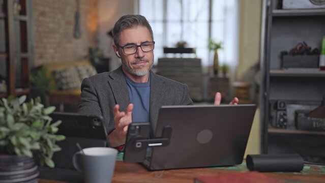Confident businessman working with laptop and digital technology at home office desk. Middle aged man, male entrepreneur talking on business video call. Telecommunication.