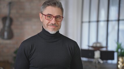 Portrait of happy casual middle aged man at home in loft room. Smart looking senior male with grey hair looking at camera in eyeglasses and turtleneck pullover, smiling.