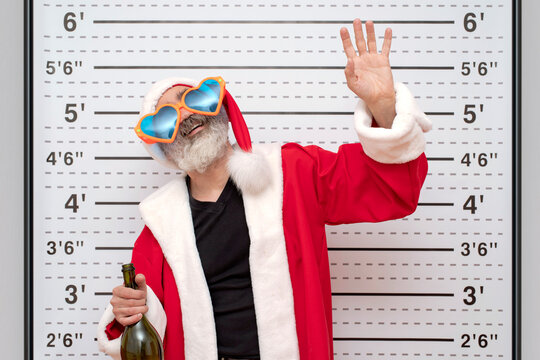 Bad Santa Claus in heart-shaped sunglasses drunkard with bottle of wine, Police Mugshot Board backdrop of a ruler with height. Natural beard, red hat, suit