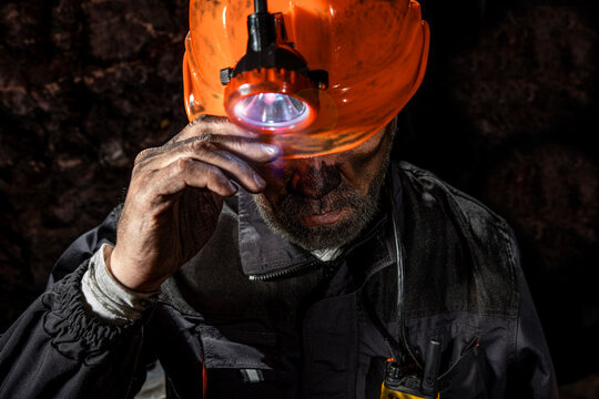 Coal miner with a dirty face in black dust, wearing a protective helmet with a flashlight and work clothes for working in a mine. Hard work underground in a coal mine, digging site.
