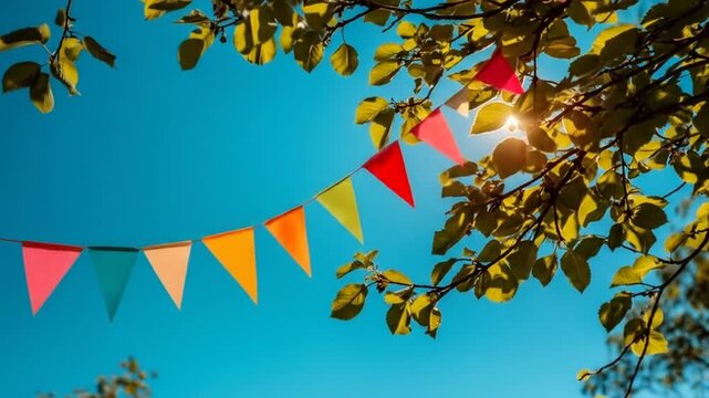 Colorful festive flags strung across a bright blue sky beneath leafy branches