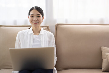 Naklejka premium Woman Sitting on Sofa Using Laptop in Bright Living Room