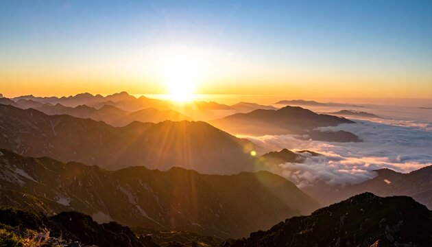Majestic sunrise paints mountain peaks with gold as clouds fill valleys. Sun bursts forth, illuminating the world below in hues of yellow and orange