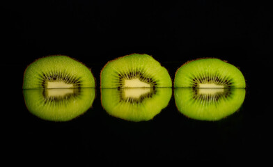 Three kiwi slices with mirroring and black background. 