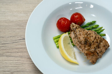 Red snapper steak, asparagus, tomatoes, and lemon on a white  plate on wooden background. Table top view.