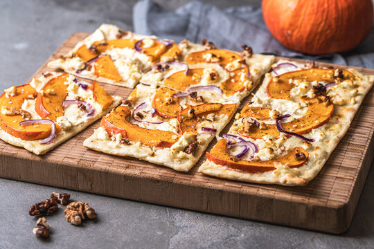 Tarte flambee with pumpkin, red onions, sheep's cheese and walnuts on a gray background