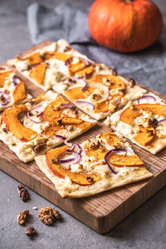 Tarte flambee with pumpkin, red onions, sheep's cheese and walnuts on a gray background