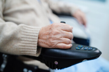 Asian elderly disability woman patient use joystick electric wheelchair in hospital.