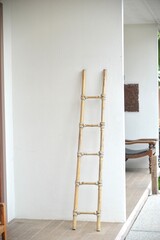 This image captures a rustic, decorative ladder crafted from natural bamboo, leaning against a clean, white wall. © CT27