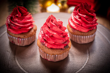 Delicious chocolate cupcakes topped with red buttercream, served on a ceramic plate with a warm festive atmosphere. Perfect sweet dessert for Christmas and New Year celebration.