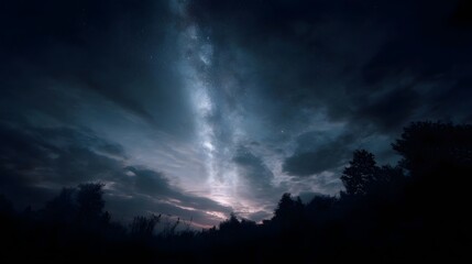 The Milky Way galaxy stretches across a cloudy night sky above a silhouetted forest