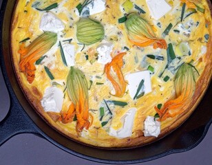 A frittata is baked in a cast iron skillet. The frittata contains squash blossoms, cheese, and green onions.