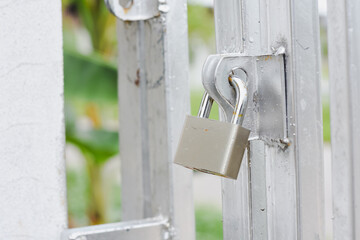 Padlock securing a silver metal gate with a blurred background.