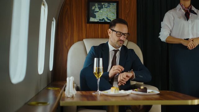 Confident successful businessman checking his watch while waiting for takeoff on a luxurious private jet, with a flight attendant standing nearby, enjoying the exclusive first-class experience