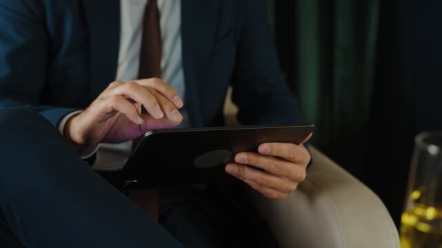 Focused businessman in a formal suit working on a digital tablet while sitting comfortably on a luxurious private jet, checking financial charts and company reports during his business trip