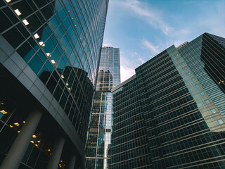 Naklejka premium Looking up at modern skyscrapers with glass facades against a partly cloudy afternoon sky in the financial district