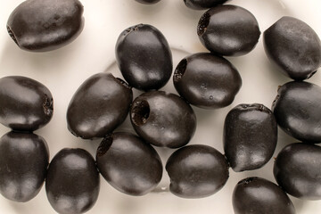 Canned pitted black olives on a ceramic plate, top view.