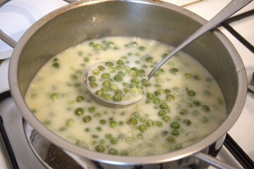 Traditional Hungarian green pea stew served in a cooking pan with a ladle, close-up view. Comfort homemade food, natural condition.