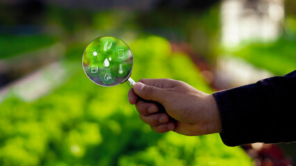 Hand holding magnifying glass with smart farming icons, representing agricultural data analysis,...