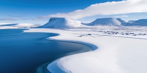 A serene winter landscape featuring snow-covered mountains and a calm blue water body, reflecting the clear sky.