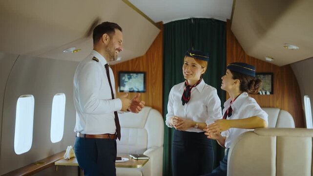 Handsome male pilot talking and laughing with two female flight attendants inside the luxurious cabin of a private jet, enjoying a friendly conversation during a break from their duties