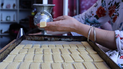 Halwa Lbouq (Moroccan Horn Pastry) - Batch of Sesame-Coated Pastries Ready to Bake, Woman Shaping Raw Dough with Traditional Cookie Press, Silver Bracelets, Home Baking Setup for Eid/Ramadan