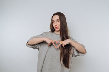 Young woman making a heart shape with her hands against a plain background.