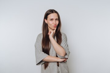 Woman with long hair in a gray shirt pondering with finger on chin
