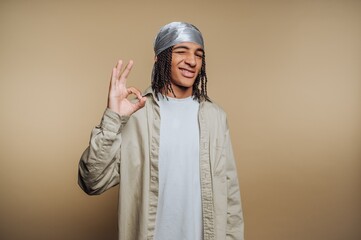 Young man with braided hair making an OK gesture, smiling.