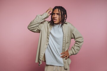 Confused Young Man with Braided Hair Against Pink Background
