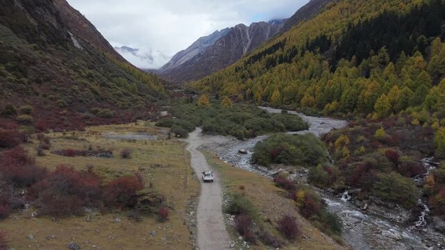 Aerial Tracking Drone Shot of Off-Road Vehicle Driving Through Autumn Mountain Valley Western Sichuan, China