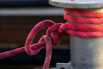 Metal Bollard on Wooden Dock with Red Rope Securely Wrapped, Fastening a Boat in a Rustic Marina Setting with Soft Background