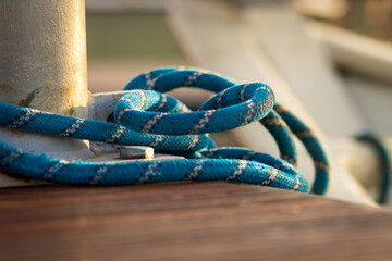 Securely Fastened Blue Rope Wrapped Around Metal Bollard on Wooden Dock, Nautical Knot Holding Boat in Place at Marina