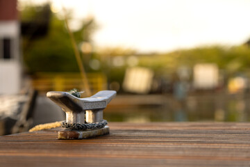 Metal Mooring Cleat on a Wooden Dock, Aged and Weathered, Set Against a Blurred Green Background with Soft Bokeh Lights