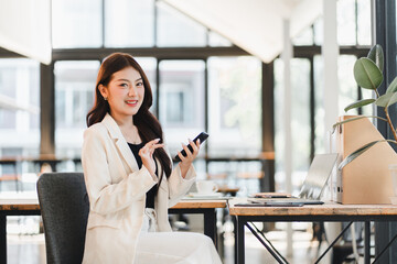 Happy smiling professional asian businesswoman using smartphone with laptop modern office. Confident young woman working desk with technology