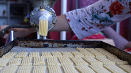 Halwa Lbouq (Moroccan Horn Pastry) - Batch of Sesame-Coated Pastries Ready to Bake, Woman Shaping Raw Dough with Traditional Cookie Press, Silver Bracelets, Home Baking Setup for Eid/Ramadan