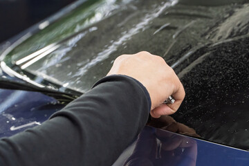 Male car service worker glue window tinting in luxury car detailing car repair the concept of love for cars and protection. Applying tinting foil on a car window in the tuning studio close-up. 