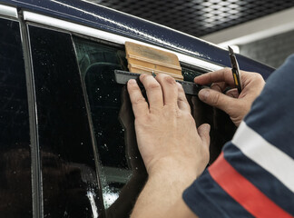 Male car service worker glue window tinting in luxury car detailing car repair the concept of love for cars and protection. Applying tinting foil on a car window in the tuning studio close-up. 