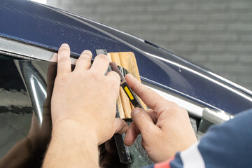 Male car service worker glue window tinting in luxury car detailing car repair the concept of love for cars and protection. Applying tinting foil on a car window in the tuning studio close-up. 