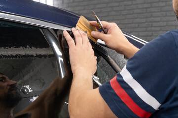 Male car service worker glue window tinting in luxury car detailing car repair the concept of love for cars and protection. Applying tinting foil on a car window in the tuning studio close-up. 