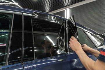 Male car service worker glue window tinting in luxury car detailing car repair the concept of love for cars and protection. Applying tinting foil on a car window in the tuning studio close-up. 